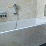 Badezimmer mit Badewannenverkleidung in hellbeiger Onyx-Optik, Wandfliesen mit integrierter Ablagefläche und schwarzen Bodenfliesen – handwerkliche Umsetzung von Madak.