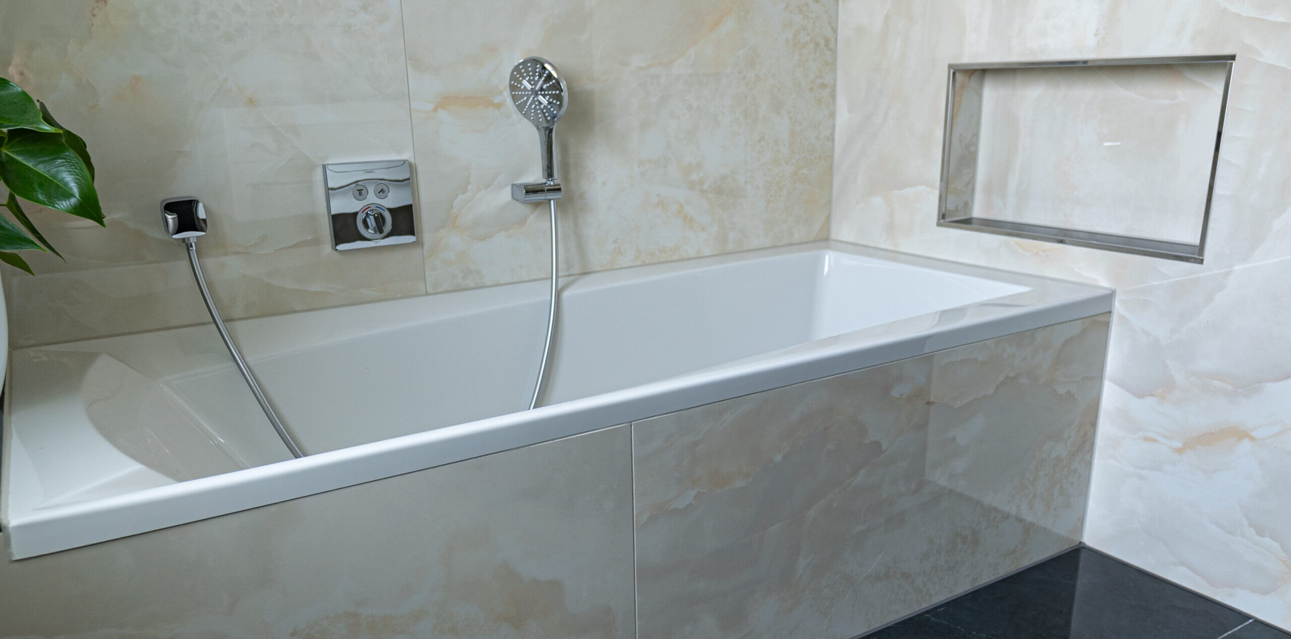 Badezimmer mit Badewannenverkleidung in hellbeiger Onyx-Optik, Wandfliesen mit integrierter Ablagefläche und schwarzen Bodenfliesen – handwerkliche Umsetzung von Madak.