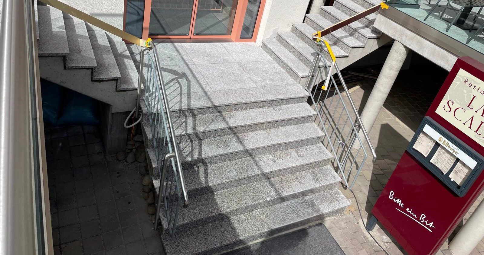 Treppenhaus Außenbereich für Restaurant. Granitstufen zu einem Podest mit zum Eingang eines Restaurants und anschließend zwei weitere Granitstufen jeweils nach links und rechts zu den Terrassen des Restaurants