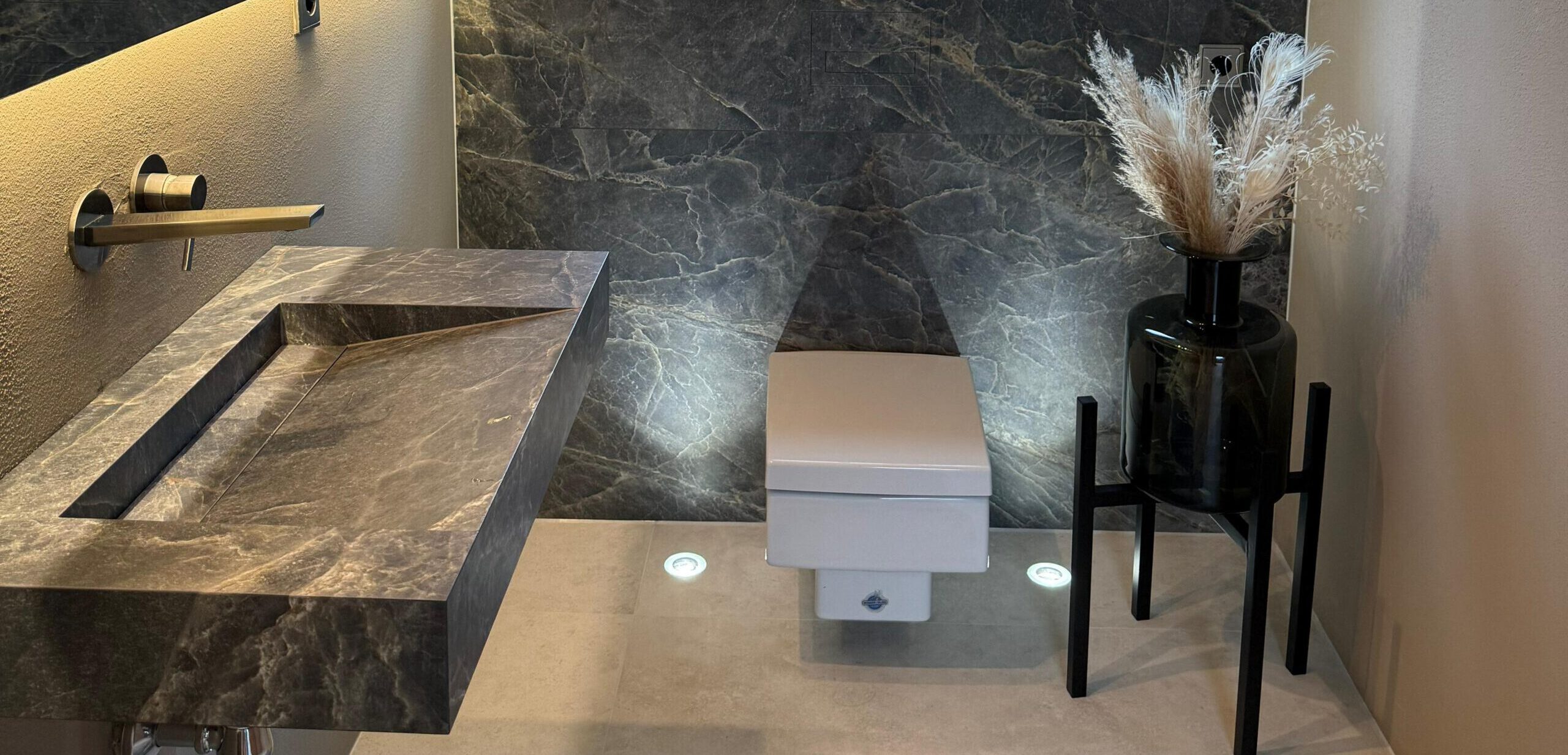 Exklusives Badezimmer mit maßgefertigtem Waschbecken, WC-Rückwand und befliesbaren WC-Drückerplatten in Natursteinoptik – gesamtes Design von Madak.