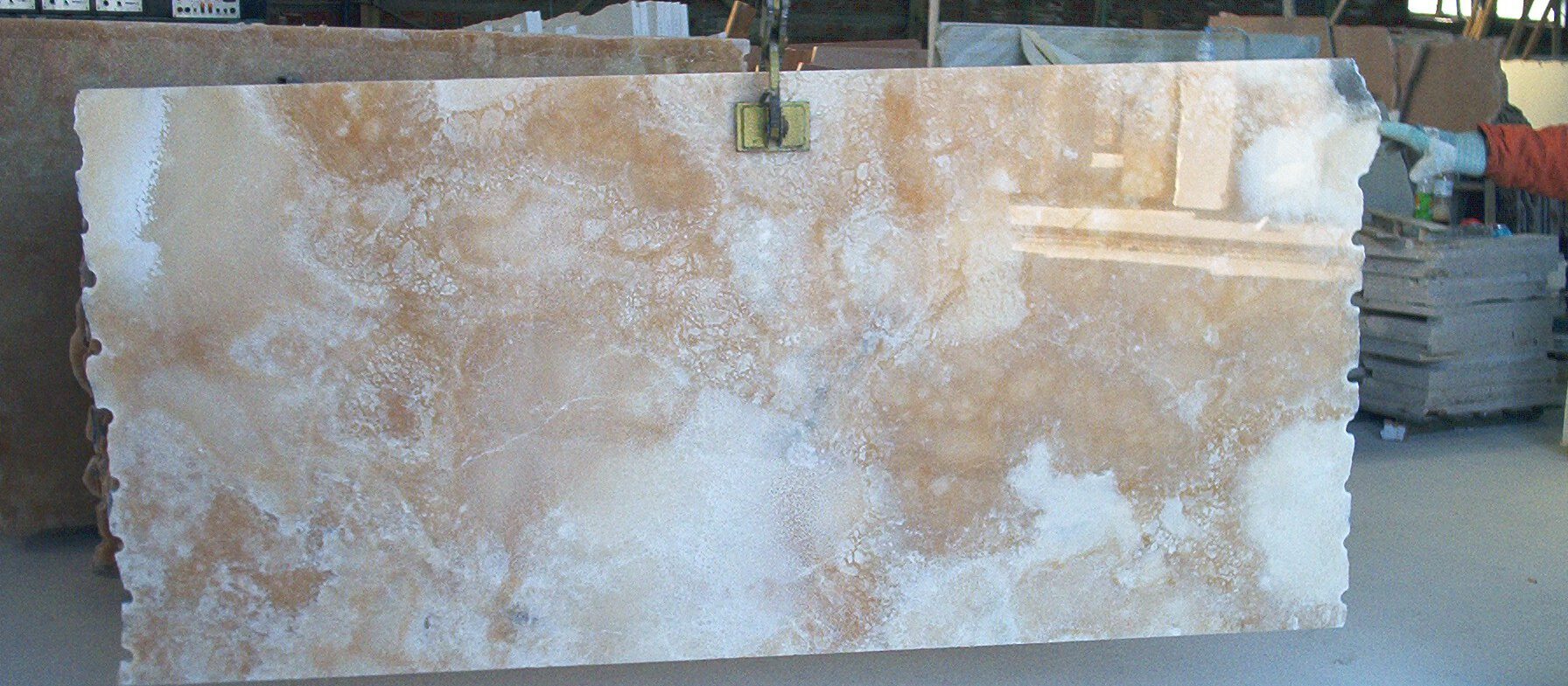 Natursteinplatte 160 × 320 cm in der Werkstatt hochkant von Kran gehalten – weiße Onyxplatte mit beigen und hellgoldenen Maserungen, transluzent.