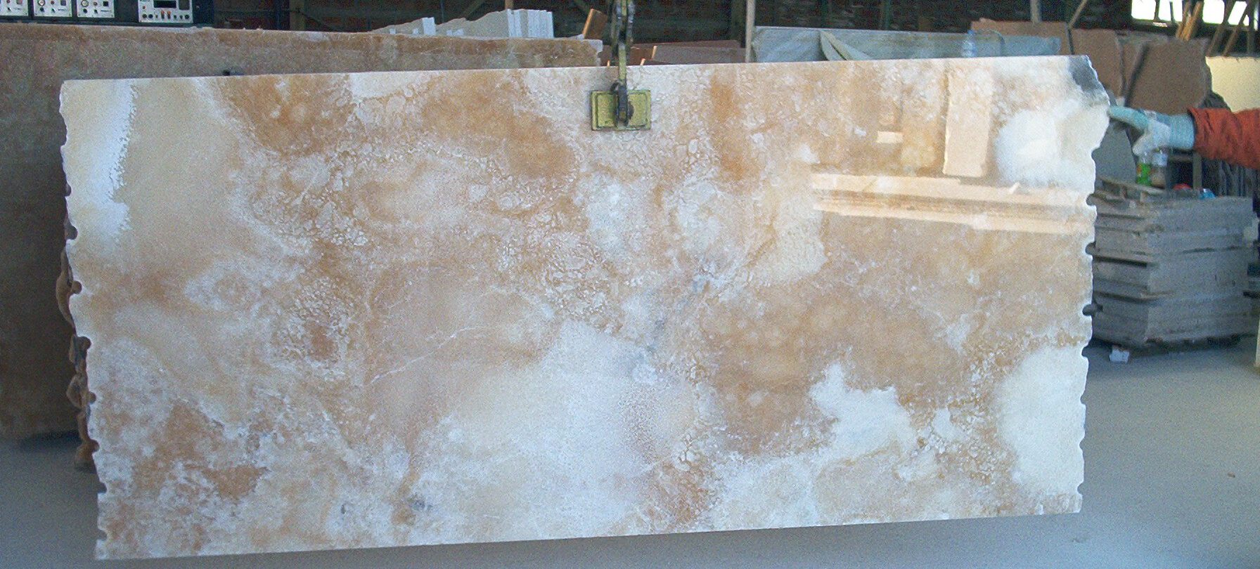 Natursteinplatte 160 × 320 cm in der Werkstatt hochkant von Kran gehalten – weiße Onyxplatte mit beigen und hellgoldenen Maserungen, transluzent.