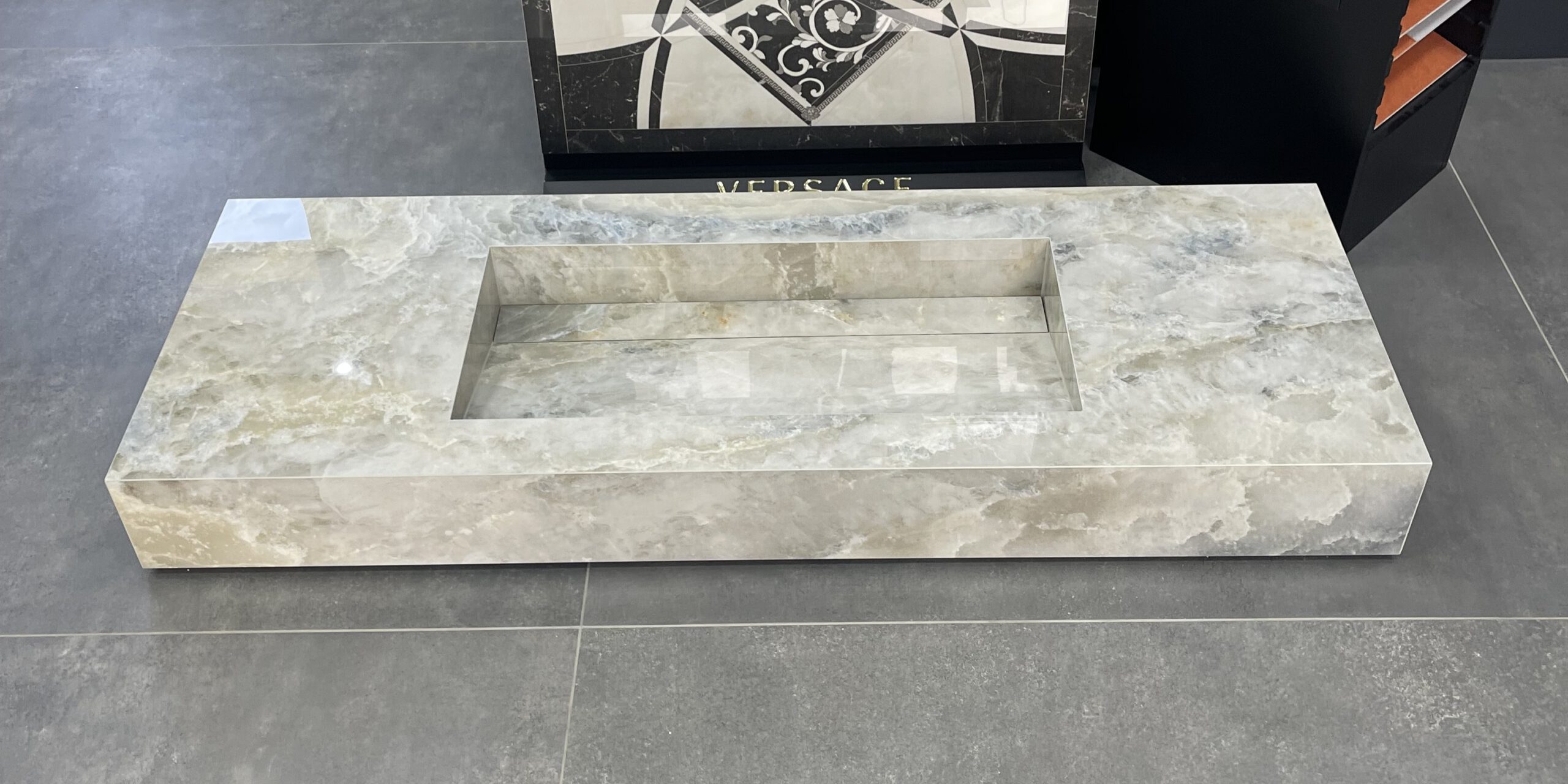 Maßgefertigtes Einzelwaschbecken 140x50x10 cm mit seitlichen Ablageflächen, gefertigt nach Kundenwunsch, verkleidet mit polierten Onyxoptik Fliesen.