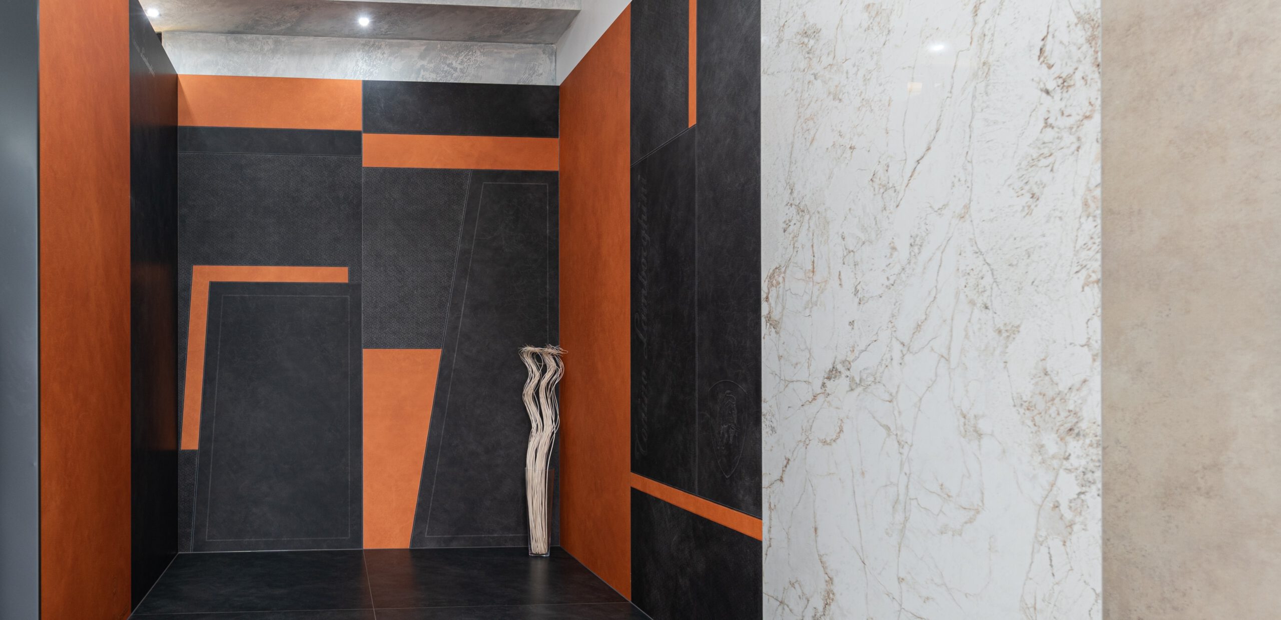 Fliesenausstellung am Standort Wetzlar: Lamborghini-Großformatfliesen 120 × 280 cm in Orange und Anthrazit, daneben Marmoroptik-Fliesen in Weiß mit goldenen Maserungen.